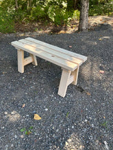 Load image into Gallery viewer, A light natural wood garden bench with a slatted backrest and solid legs, placed outdoors on a gravel path with trees and greenery in the background.