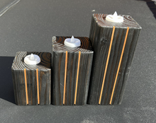 Load image into Gallery viewer, Three rectangular dark wood candle holders with vertical orange stripe accents and white faux flame tops, arranged by size on a gray asphalt surface.