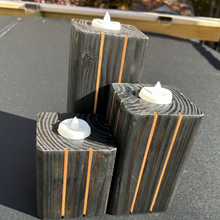 Load image into Gallery viewer, Three dark wood block candle holders with vertical orange stripes and white LED tea light candles, arranged on a dark tabletop outdoors.
