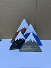 Load image into Gallery viewer, Four triangular wooden mountain decorations with painted snow-capped peaks, displayed on a light surface against a brown cardboard background.
