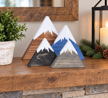 Load image into Gallery viewer, Three painted wooden mountain decorations with white snowy peaks are arranged on a rustic wooden mantel. The mountains have different wood-grain finishes in black, gray, and brown, with blue and white painted sections.