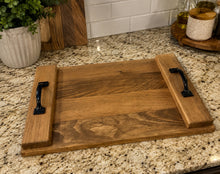 Load image into Gallery viewer, A rectangular wooden serving tray with two raised side panels and black metal handles, placed on a granite kitchen countertop.