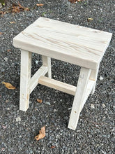Load image into Gallery viewer, A small, square wooden stool with a whitewashed finish and natural wood grain, shown outdoors on a gravel surface.
